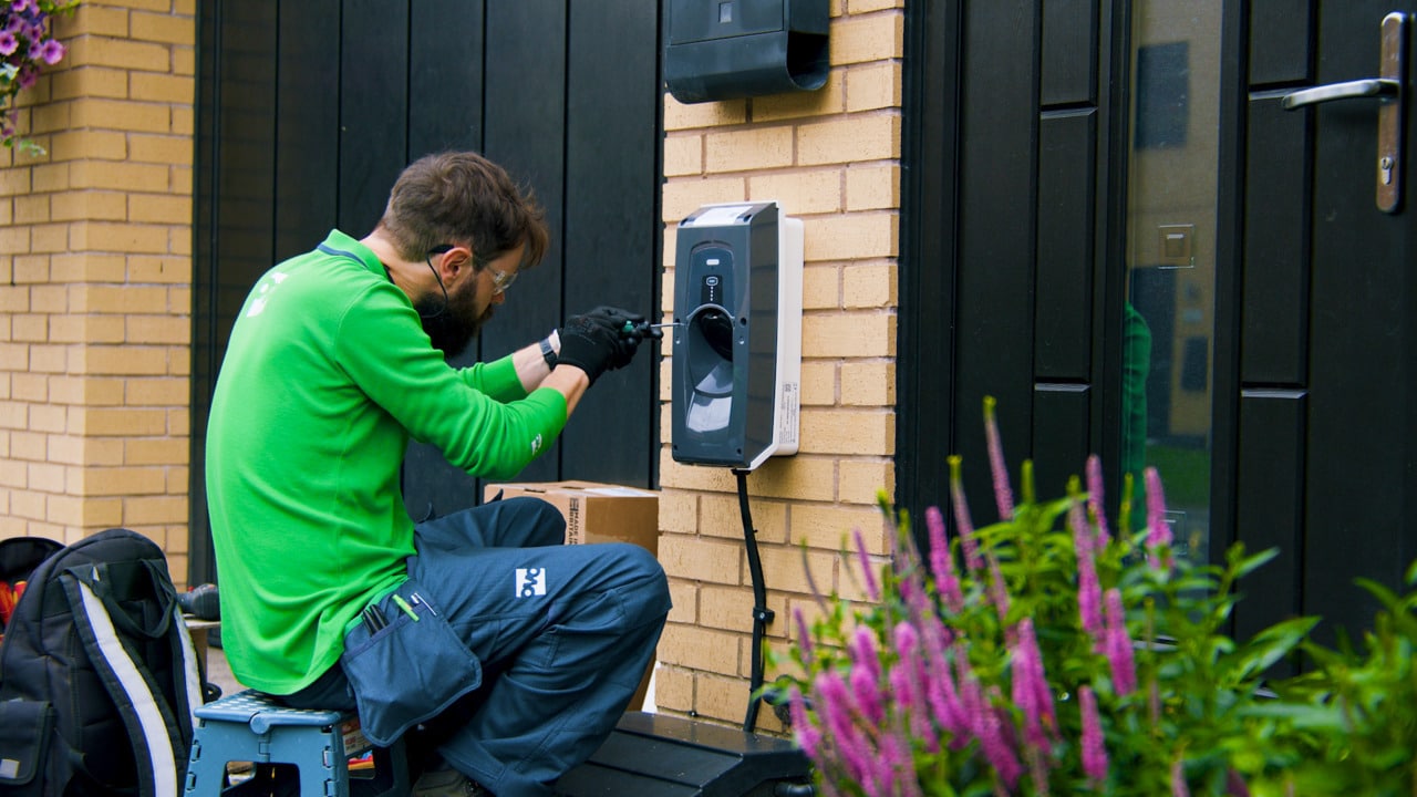 An engineer in a green uniform installing a home electric vehicle charge point on a brick wall