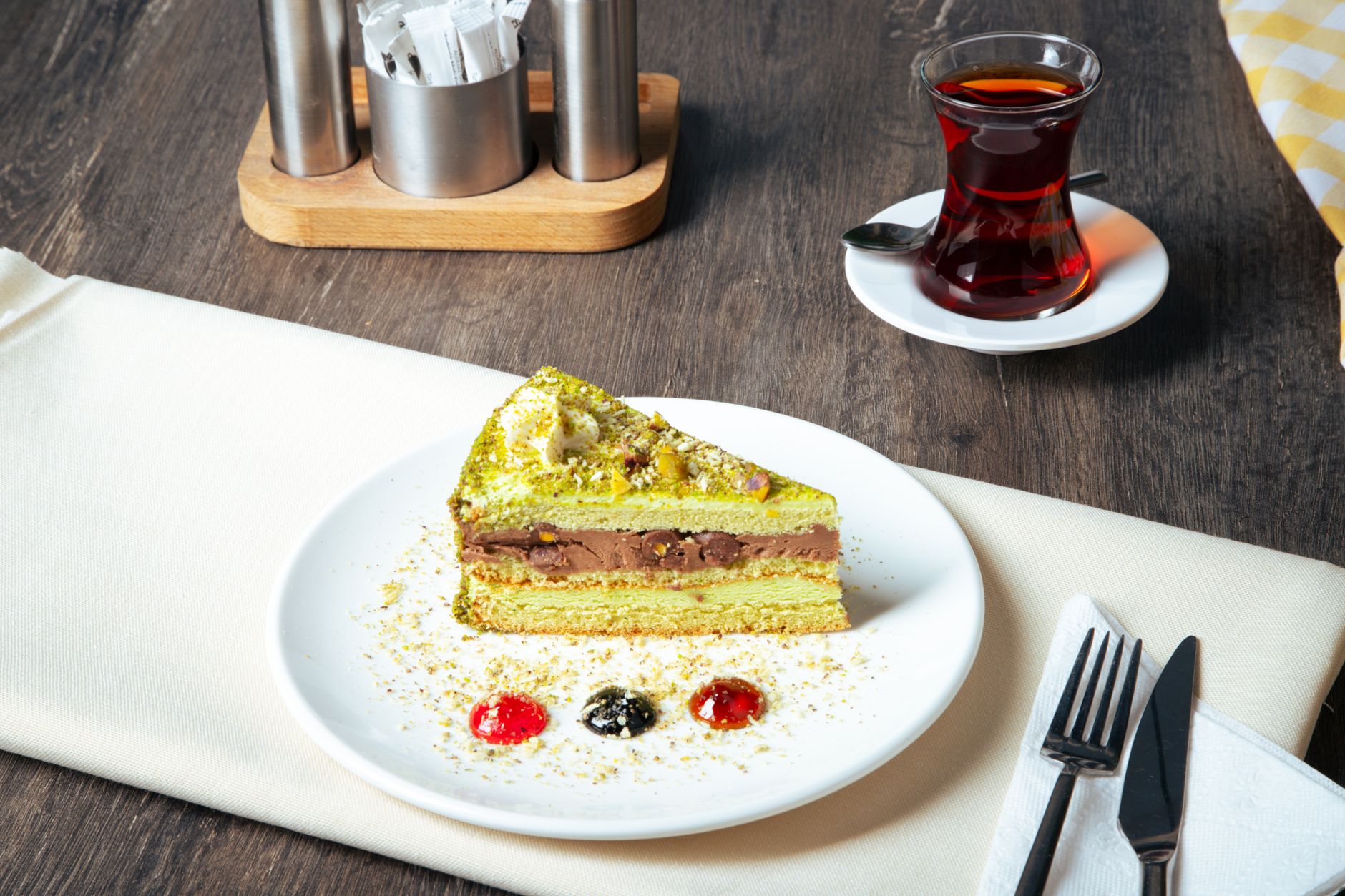 Part de gâteau vert à la crème au chocolat sur une assiette blanche, avec un verre de thé noir sur soucoupe, sur une table en bois.