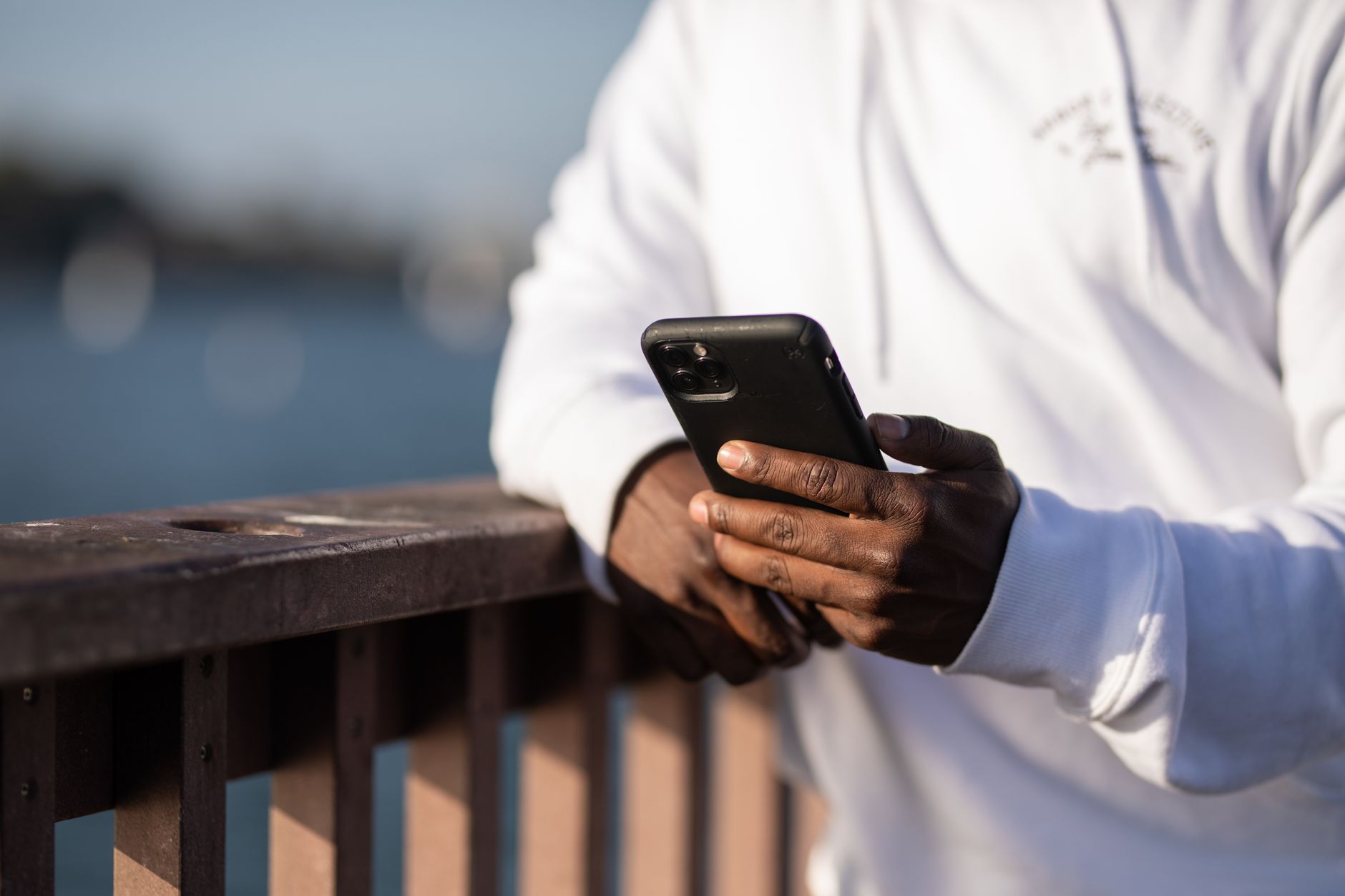 A person holding and looking at a black smartphone outdoors next to a railing