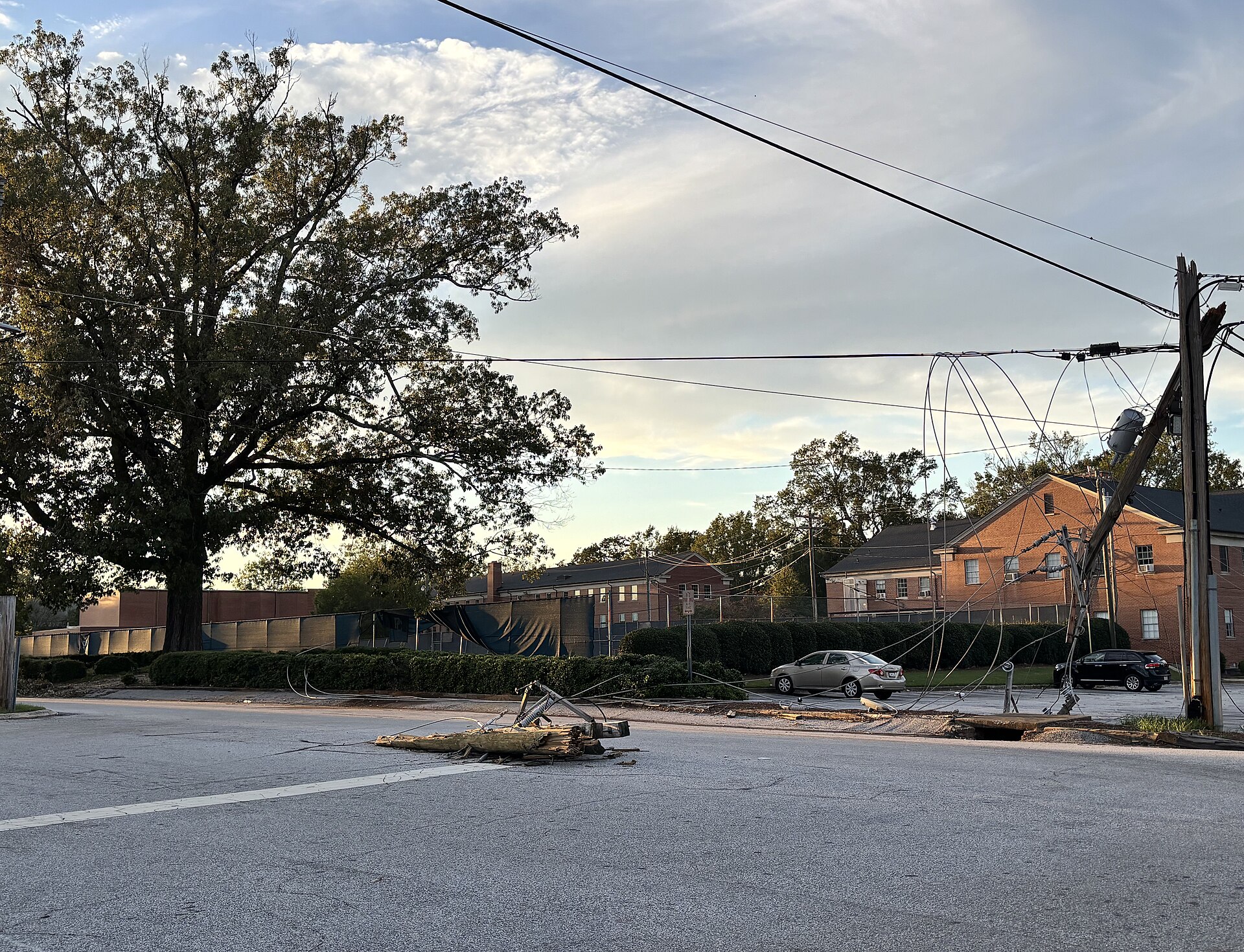 Snapped utility pole and downed power lines lying across a street after a storm